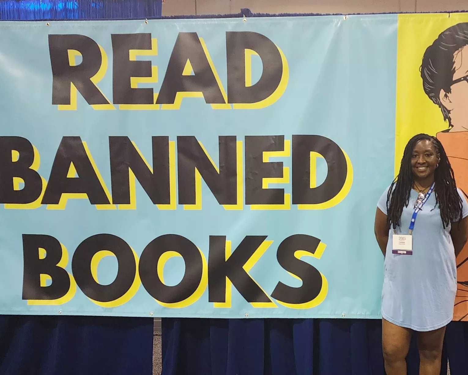 Member Cassie Owens Moore poses in front of a banner that says "Read Banned Books."